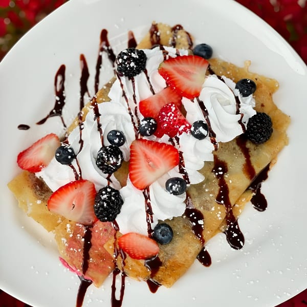 Vegan crepe topped with whipped cream, fresh strawberries, blueberries, blackberries, and chocolate drizzle.