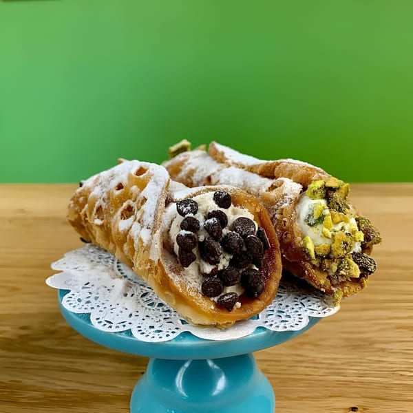 Three vegan cannolis, one with chocolate chips, another with pistachios, on a blue cake stand.