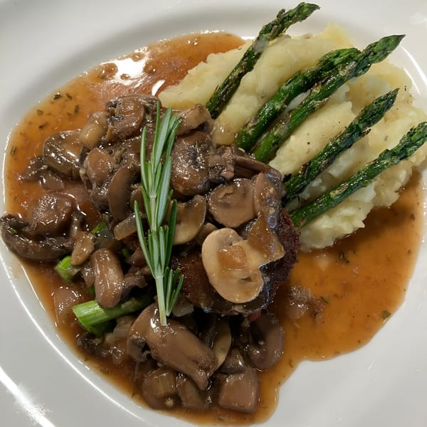 Vegan mushroom steak with gravy, mashed potatoes, and asparagus, garnished with rosemary.