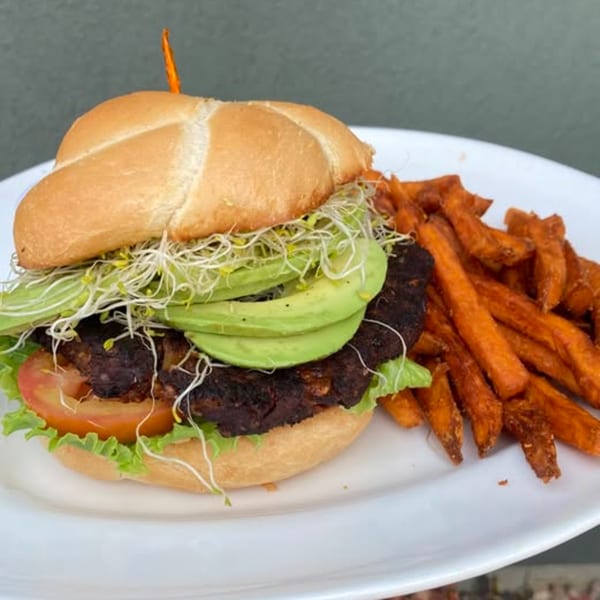 Vegan burger with avocado, sprouts, lettuce, and tomato, served with sweet potato fries.